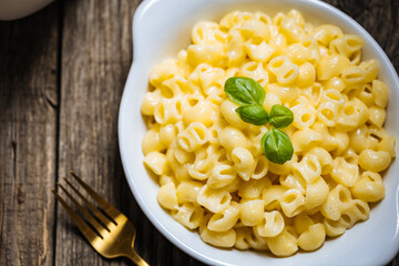 Mac and Cheese in blue bowl placed on rustic wooden board, with basil on top. 