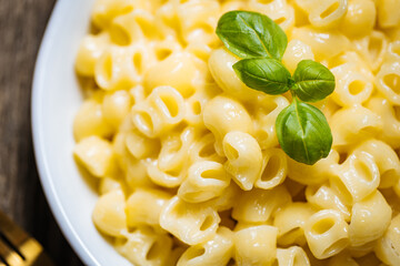 Mac and Cheese in blue bowl placed on rustic wooden board, with basil on top. 