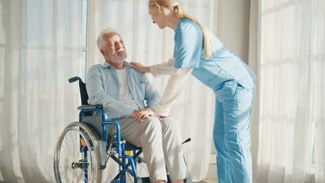 Caregiver in hospital helping an elderly patient for support in clinic. Medical nurse talking to a senior person with disability.Male person with a disability patient receives support and medical care