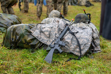 Modern black training military rifle leaning against a wet ruck backpack
