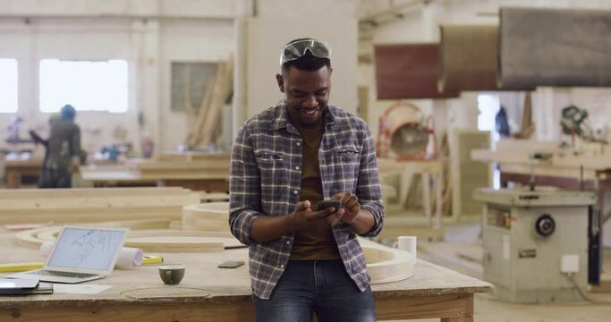 Phone, internet and black man carpenter in a workshop search online, web and website working on wood project. Entrepreneur, app and African worker or employee streaming funny social media and smile