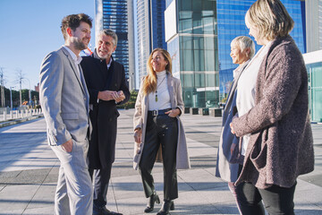 Group of coworkers outside in front of office buildings discuss about business plan.