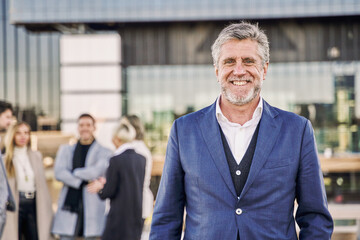 Fototapeta na wymiar portrait of middle-aged gray-haired businessman posing with a group of his company's workers in the background
