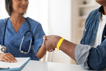 Doctor shaking hands with male patient wearing hospital wristband during medical appointment - obrazy, fototapety, plakaty