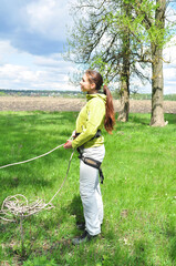 An athletic girl climbs a tall tree using a carabiner belay, pulls herself up onto the rope with her hands, and gains great height. Recreation and sports.