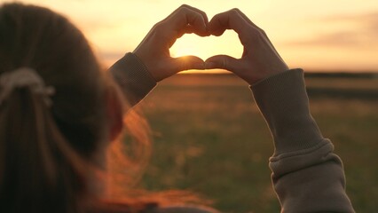 Young woman loves to travel. Girl molded love heart from her palms. Happy girl making heart shape with fingers. Light of summer spring sun is in my hands. Travel relax in nature. Healthy heart concept