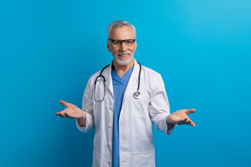 Cheerful senior doctor gesturing on blue background - obrazy, fototapety, plakaty