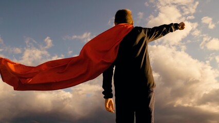 Boy child plays superhero in red cape with his hand raised to sky, child dream. Child hero in red...