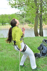 An athletic girl climbs a tall tree using a carabiner belay, pulls herself up onto the rope with her hands, and gains great height. Recreation and sports.