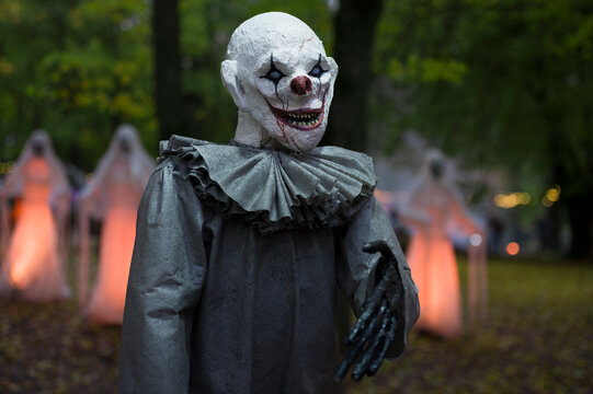 Halloween decoration, grinning clown standing on ghosts background in the forest