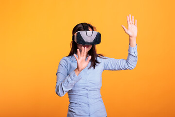 Cheerful woman wearing vr goggles enjoying 3d simultation in studio over yellow background, enjoying digital entertainment. Electronic futuristic experience with augmented tech innovation