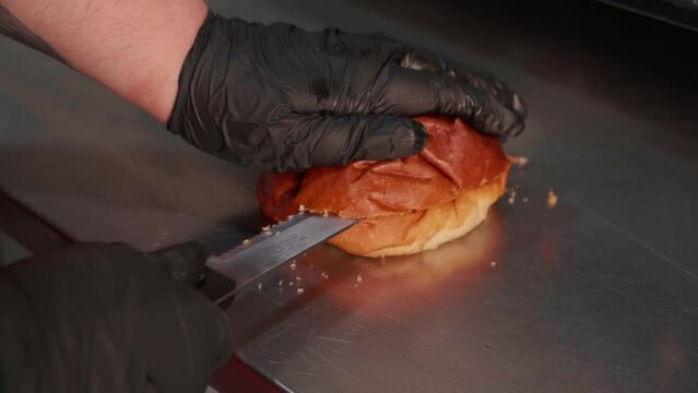 Chef in black gloves making burge. cut the burger bun. Close-up of a skilled craftsman working at the workplace 