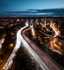 Aerial image of highway infrastructure with light trails of cars driving under old aquaduct bridge...