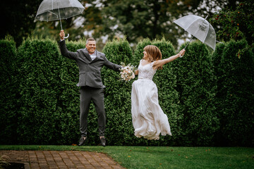 The happy couple jumps joyfully while holding a wedding umbrella, celebrating their special day...