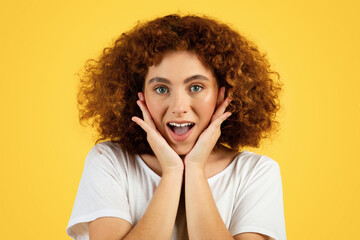 Fototapeta na wymiar Cheerful shocked teenager caucasian curly girl touching face with hands, enjoy beauty care