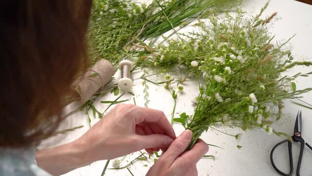 Floristic master class on weaving flower wreath for feast of Ivan Kupala.Woman weaves wreath of fresh field herbs and flowers,pagan symbol,solstice day.Rustic style.Wreath of daisies and herbs,summer