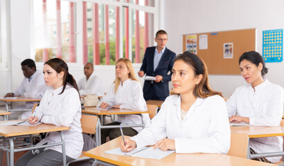 Multiethnic group of adult medical students attentively listening to lecture in classroom