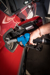 man hand refueling gasoline and filling the tank at the gas station or petrol station pump to the red car - obrazy, fototapety, plakaty