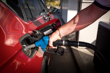 man hand refueling gasoline and filling the tank at the gas station or petrol station pump to the red car - obrazy, fototapety, plakaty