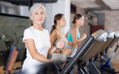 Elderly athletic woman in sportswear training on treadmill in gym