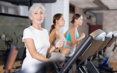 Fototapeta premium Elderly athletic woman in sportswear training on treadmill in gym