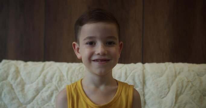 Portrait Funny little boy smiling child looking at camera are sitting on the couch at home, cute kid child with pretty face sitting on sofa. Concept of a happy childhood.