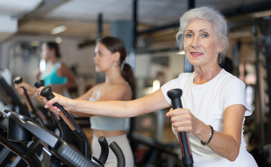 Fototapeta premium Mature sportswoman training at elliptical machine in modern gym