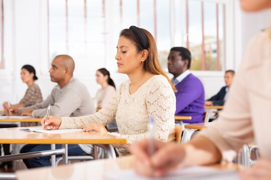 Young positive woman sitting at desk in classroom working during lesson at adult education class