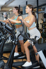 Fototapeta na wymiar Slender athletic girl during cardio exercises on elliptical simulator in fitness center. Sports to max. Electronic tracking for most productive workout