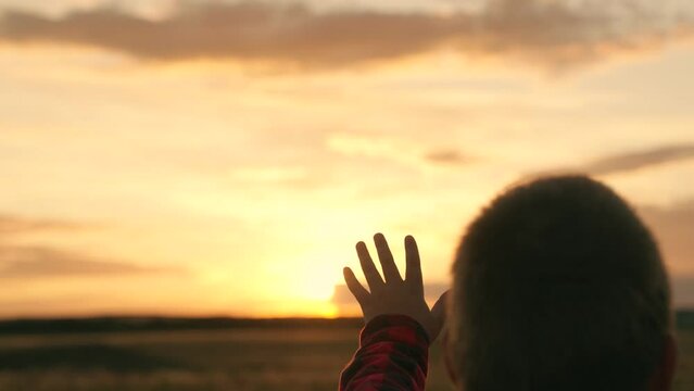 Kid Boy stretches his hand to beautiful sky, dream in nature. Child is playing. Hand of child boy stretches to beautiful sky, sunset. Children dream hopes, reach out your hands to sky. Children prayer
