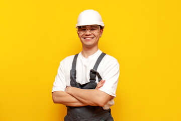 asian male builder in uniform standing with arms crossed and smiling on yellow isolated background