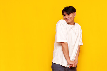 modest young asian guy in a white t-shirt is shy and embarrassed on a yellow isolated background - obrazy, fototapety, plakaty