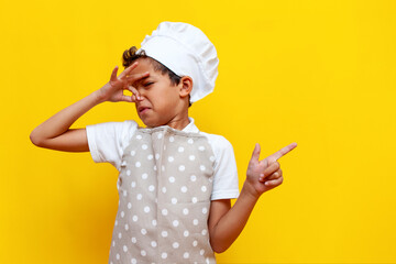 little chef child african american in uniform covers nose with hand from bad smell on yellow...