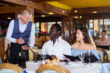 Fototapeta na wymiar Waiter making recommendation to positive couple having date in restaurant