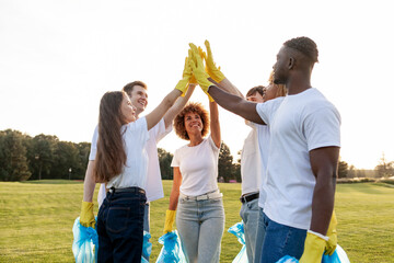 group of multiracial people in gloves with garbage bags high-fiving and celebrating success together in the park