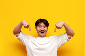 young asian guy in white t-shirt pointing with hands down on yellow isolated background