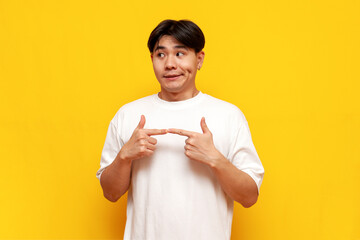 modest young asian guy in white t-shirt feeling shy on yellow isolated background