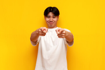 I choose you. young asian guy in a white t-shirt points with his hands at the camera and smiles - obrazy, fototapety, plakaty