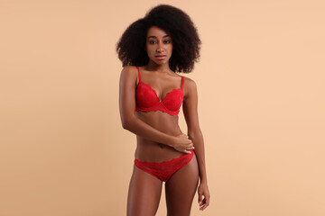 Fototapeta premium Beautiful woman in elegant red underwear on beige background