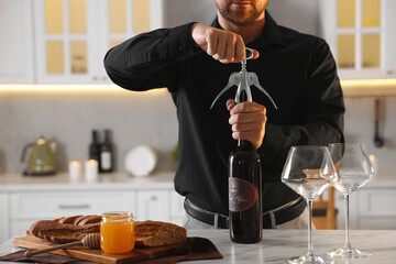 Romantic dinner. Man opening wine bottle with corkscrew at table in kitchen, closeup - obrazy, fototapety, plakaty