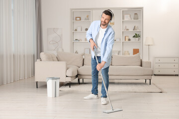 Enjoying cleaning. Man in headphones listening to music and mopping floor at home