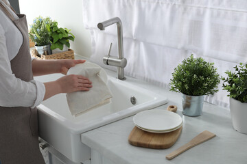 Woman wiping plate with towel above sink in kitchen, closeup