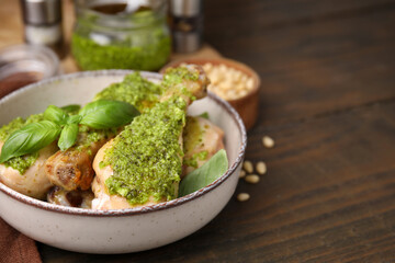 Delicious fried chicken drumsticks with pesto sauce and basil in bowl on wooden table. Space for text