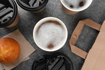 Coffee to go. Paper cups with tasty drink and muffin on grey table, flat lay