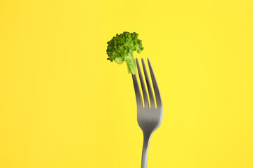 Fork with tasty broccoli on yellow background