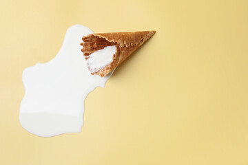 Melted ice cream and wafer cone on beige background, top view. Space for text