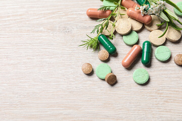 Different pills and herbs on wooden table, above view with space for text. Dietary supplements