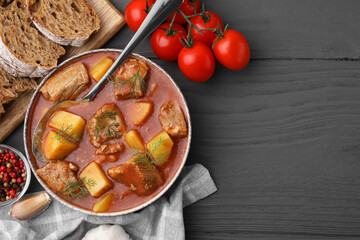 Delicious goulash in bowl and ingredients on dark wooden table, flat lay. Space for text