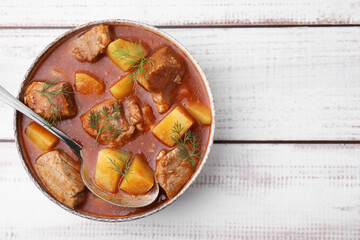 Delicious goulash in bowl on white wooden table, top view. Space for text