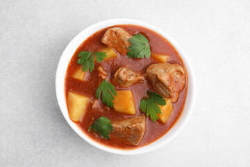 Delicious goulash in bowl on light grey table, top view